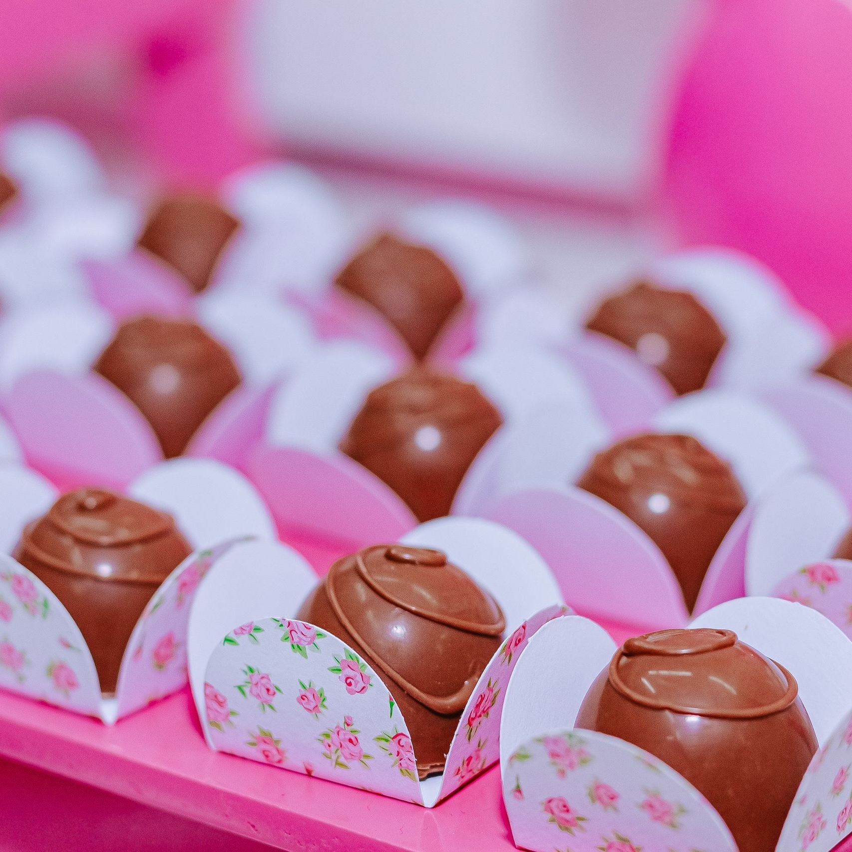 Beautifully arranged chocolate truffles in floral wrappers on a pink background. Perfect for celebrations.