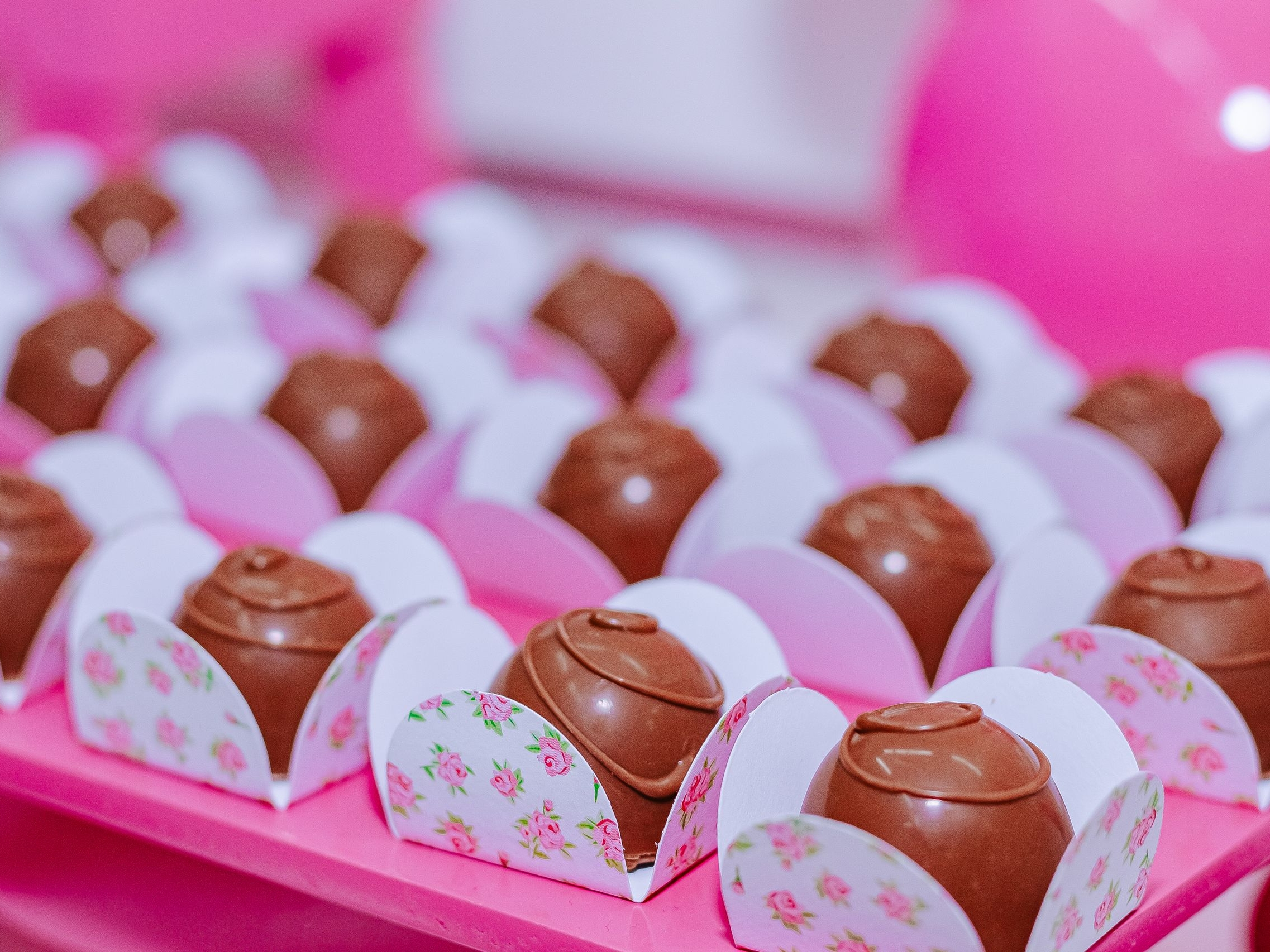 Beautifully arranged chocolate truffles in floral wrappers on a pink background. Perfect for celebrations.
