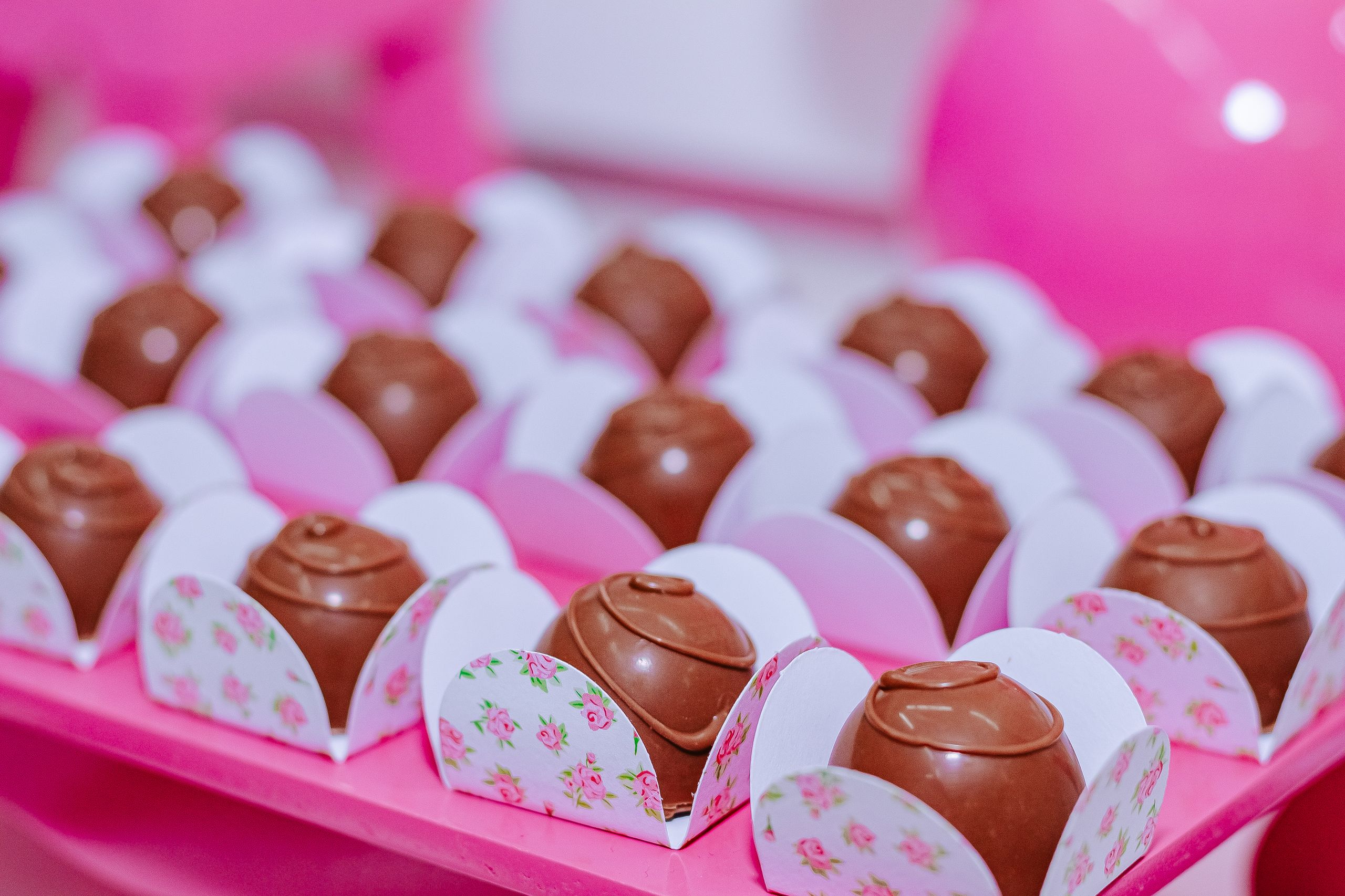 Beautifully arranged chocolate truffles in floral wrappers on a pink background. Perfect for celebrations.